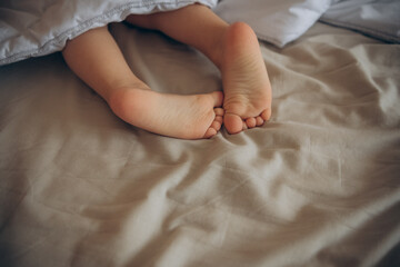 Children's legs stick out from under the warm blanket