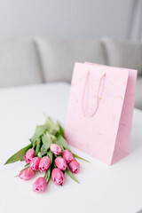 A bouquet of pink fresh tulips lies on a beige fabric and a pink gift bag. Valentine's Day background