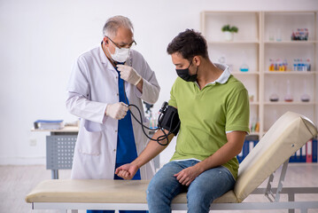 Fototapeta premium Old male doctor measuring young patient's blood pressure