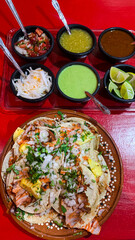 Order of pastor tacos on a red table with sauces and seasonings on the side