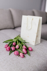 A bouquet of pink fresh tulips lies on a beige fabric and a white gift bag. Valentine's Day background