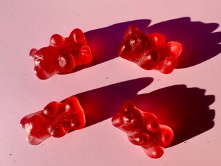 Pink cranberry flavored gummy bears illuminated by sunlight with shadows cast over pink surface  - 570456854