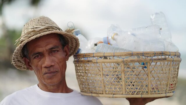 Serious senior asian man volunteer cleans beach from plastic bottles. Portrait