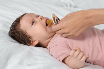 Mother giving pacifier to crying little baby on bed, closeup