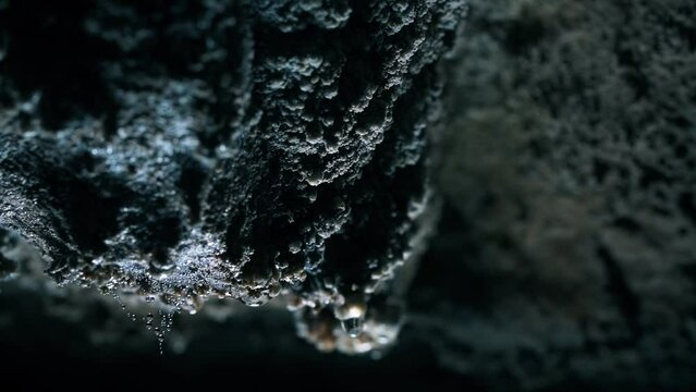 Dolly shot of drops dripping from rocks in cave
