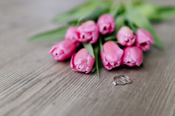 Pink tulips and engagement rings with diamonds lie on a wooden background. Background for Valentine's Day. Gift for Mother's Day or Women's Day