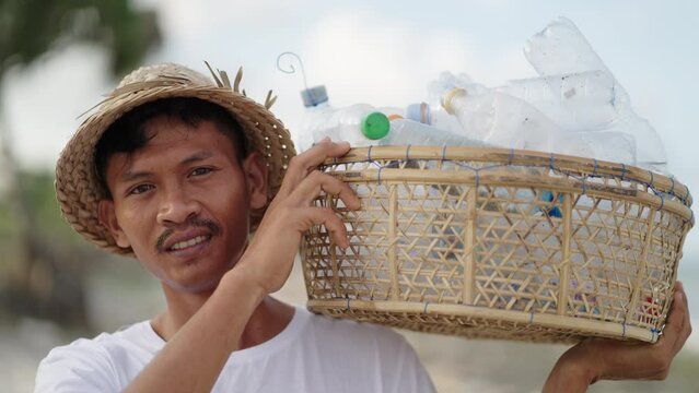 Proud young asian man volunteer cleans beach from plastic bottles and ocean trash. Medium portrait