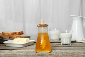 Jar of tasty honey, milk, butter and bread on wooden table