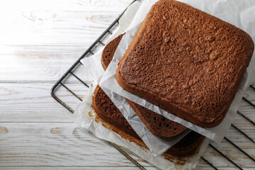 Layers of homemade chocolate sponge cake on white wooden table. Space for text