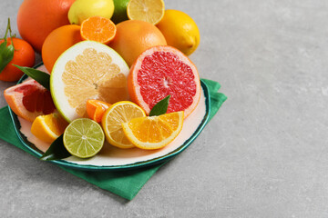 Plate with different citrus fruits and fresh leaves on light grey table. Space for text