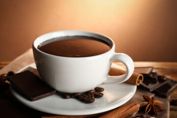 Cup of delicious hot chocolate, spices and coffee beans on wooden table