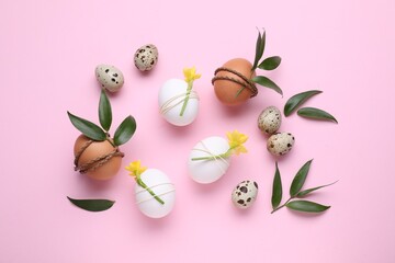 Easter eggs decorated with green leaves and flowers on pink background, flat lay