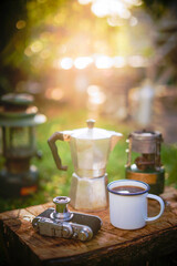 Black coffee in a white enamel mug on old wooden background with a film camera and coffee equipment Camping in the forest in the morningม selective focus, soft focus.