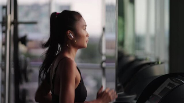 Attractive asian girl runs on treadmill in gym. Asian woman workout for weight loss in slow motion
