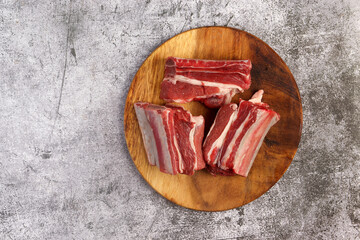 Raw beef ribs on a cutting wooden board on a dark grey background. Top view, flat lay
