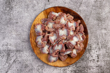 Raw chicken gizzards on a round wooden cutting board on a dark grey background. Top view, flat