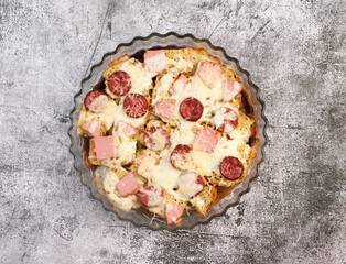Cheese sausage strata casserole in a glass baking dish on a dark grey background. Top view, flat lay