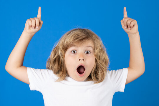 Surprised Kid Pointing Up Finger On Blue Studio Background. Shocked Kid Pointing To Copyspace, Showing Promo Offers, Points Away. Excited Emotions, Shock, Omg And Wow Expression.