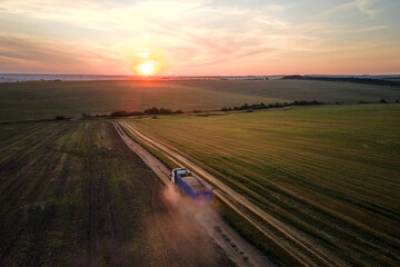 Aerial view of cargo truck driving on dirt road between agricultural wheat fields making lot of...