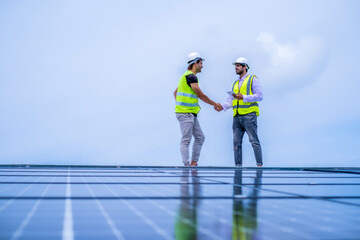Two engineer checking hand each other after installation solar system on roof, two man in safty suit walking on roof againt blue sky and solr planel.