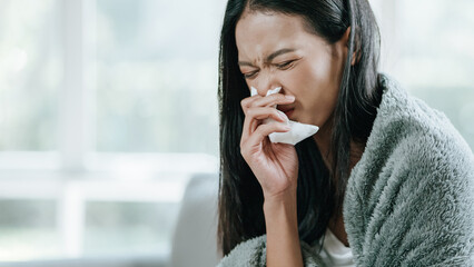 Fototapeta na wymiar Unhappy sad Asian woman in cloak suffering from fever and flu on sofa