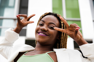 Head shot of Black woman with braided hair looking at camera showing peace sign with hands.
