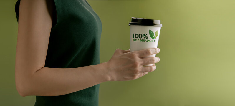 Biodegradable and Compostable Packaging Concept. Closeup of Woman Holding a Hot Cup of Coffee against a Green Wall. Zero Waste Materials. Environment Care, Reuse, Renewable for Sustainable Lifestyle