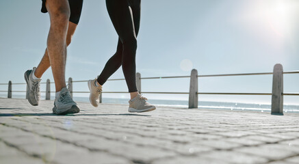 People, legs and running at the beach for exercise, cardio workout or training together outdoors. Leg of friends taking run, walk or jog on warm sunny day by the ocean coast for healthy wellness - obrazy, fototapety, plakaty