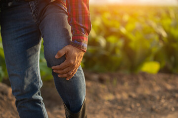 Injuries or Illnesses, that can happen to farmers while working. Man is using his hand to cover over knee because of hurt,  pain or feeling ill.