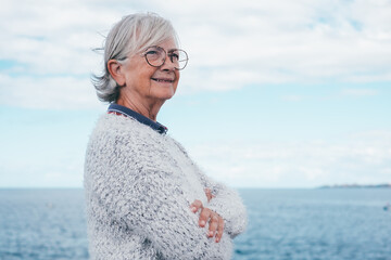 Portrait of pensive handsome senior woman standing by the sea looking away. Smiling elderly...