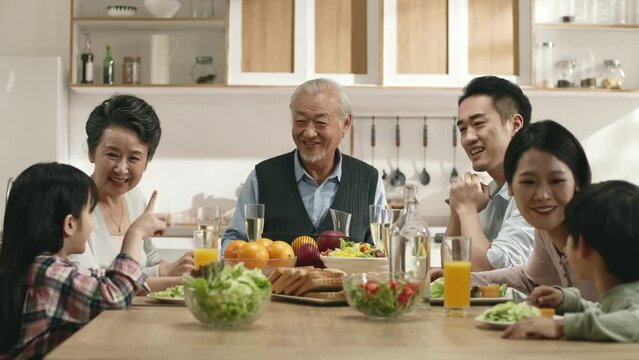 happy middle class three generation asian family sitting at table eating meal enjoying conversation
