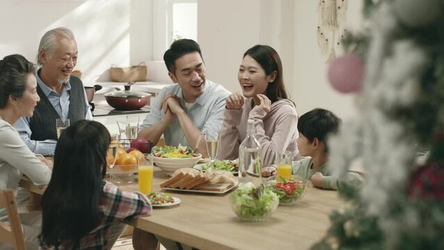happy middle class three generation asian family sitting at table eating meal on christmas day