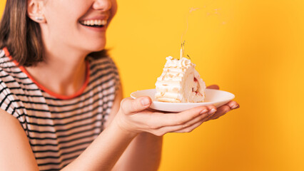 Lady in front of yellow background holding plate with piece of cake in her hands.