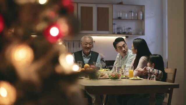 happy three generation asian family sitting at table having a toast while eating dinner during christmas reunion