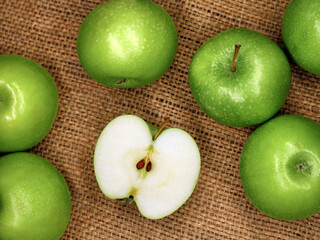 Ripe green apples and a sliced half of an apple on burlap sack, top view of healthy juicy fruits
