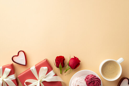 St Valentine's Day concept. Top view photo of red gift boxes with ribbon bows heart shaped candles cup of coffee plate with meringue and red roses on isolated beige background with blank space