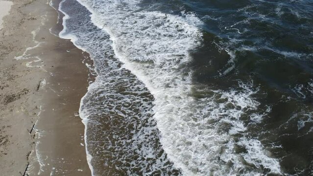 Sea waves from above. Sea waves with white foam rolling on sandy beach of the seashore coast on sunny day. Flying over sandy beach. Top view. View from above. Seascape waterscape. Aerial drone view