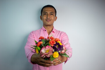 Portrait of Asian young man holding flower wearing pink shirt isolated on white background.