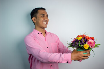 Portrait of Asian young man holding flower wearing pink shirt isolated on white background.