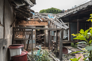 Urbex, abandoned courtyard of a traditional South-Korean neighbourhood, doors and walls are destroyed, windows are broken, there are remains on the floor, vegetation is growing, it's messy and dirty