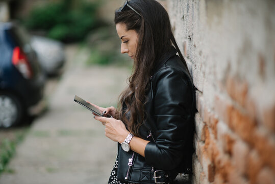 Young attractive woman by the brick wall is looking on her phone.