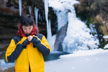 redhead young woman with red in a waterfall of nine in the mountain while snowing, copy space