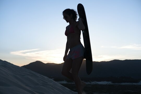 Beautiful woman walking with sandboard at her back at sunset