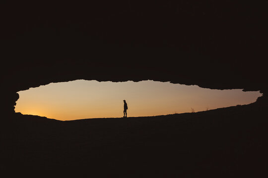 A man stands outside a rock cave by the seaside watching sunrise, Cantabria, Spain