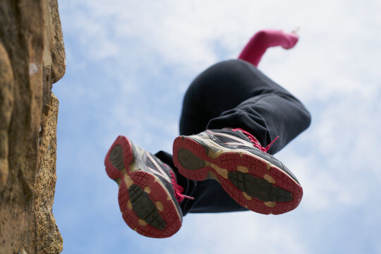 From below female in sneakers jumping from rough stone wall