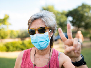 pretty white hair senior woman with mask by covid-19, victory symbol with hand