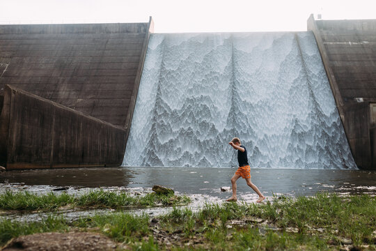 Child crossing stream in front of waterfall spillway