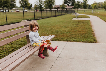 Young girl sits on bench at dog park holding autumn leaves