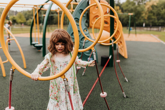 Young girl plays on playground equipment at park on cloudy day