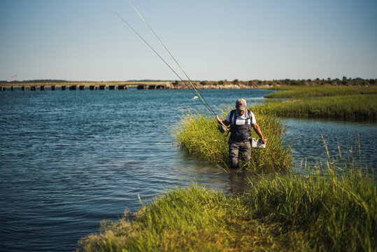 Fly fisherman wading through ocean water with sea grass